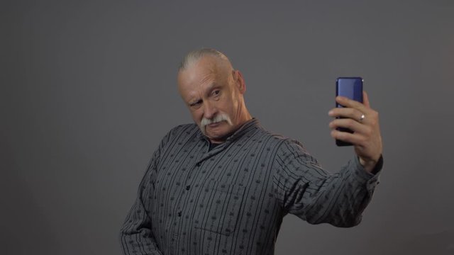handsome senior man with trendy grey mustache and ponytail poses holding modern smartphone taking photos closeup. Concept man emotion