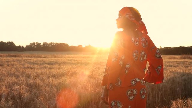 HD Video clip of African woman farmer in traditional clothes standing in a field of crops, wheat or barley, in Africa at sunset or sunrise