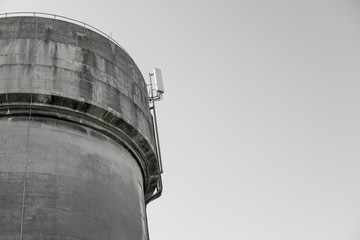 Detailed view of a large cast-concrete water tower, showing its weathering. A newly installed 5G mast can be seen atop the tower.