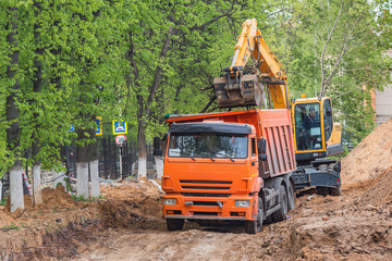 Excavator loads sawn sections of the tree trunks on the construction site.