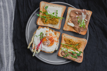 Variety of sandwiches for breakfast, snack, appetizers with fried egg, peanut paste, pea microgreen. Flat lay, top view