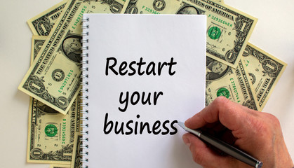 Male hand writing 'restart your business' on white note, on white background. Dollar bills.