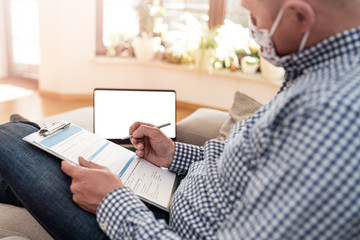 A man with an anti-bacterial mask on his face fills out a medical form for coronavirus test. He is on quarantine.