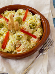 Russian salad with olives, red pepper, grated egg with mayonnaise in brown clay bowl on blue tablecloth