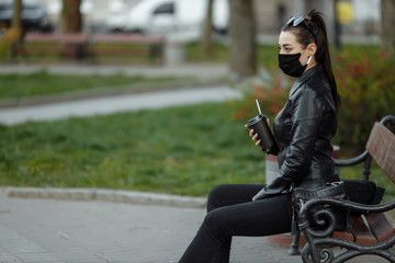 Fototapeta premium Young beautiful woman with cup of coffee wearing black medical mask