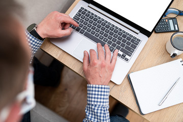 Fototapeta na wymiar Businessman's hands typing on a computer keyboard during a home office. Man wearing casual shirt using laptop in the home. Office equipment such as notes, calculator and laptop on table.