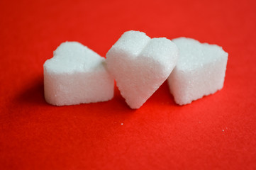 three heart shaped sugar cubes on red background closeup