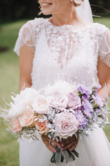 Close-up of a bride’s bouquet of roses, carnations in white, pink, violet, lavender, peach shades. The bride in a lace white dress holds a bouquet in her hands.