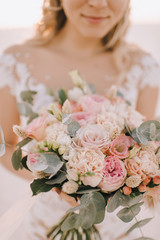 Naklejka premium Close-up of a bride's bouquet of peach roses, carnations, eucalyptus. The bride in a white dress with long sleeves holds a bouquet in her hands. 