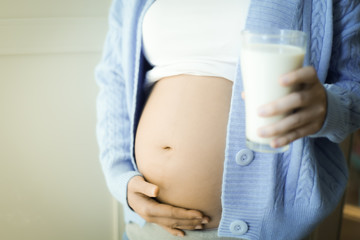 Pregnant woman wearing a blue sweater, left hand stroking the belly because of love for her child. Her right hand held a glass of milk. She has milk to supplement the calcium. Good nutrition.
