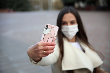 White -skinned girl in a medical mask with a phone in her hands