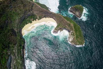 Top aerial view of the Kelingking Beach of Nusa Penida, Bali. Secluded, white sandy beach with turquoise waters enclosed by a steep cliff & headland.