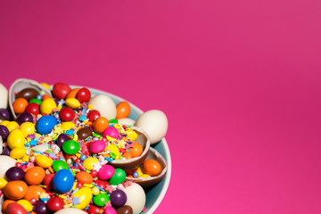 Part of a blue bowl filled with colored jelly and chocolates was shot close-up in front of saturated pink background. There is a place for text.