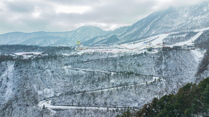 Aerial drone view of Xiling Snow Mountain, the ski resort in Sichuan next to Chengdu. The mountain curved road through the trees, place for skiing and tourist base. Winter sports time.