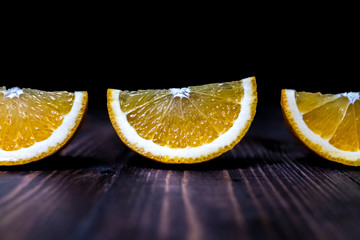 Three orange slices lie on a wooden surface on a dark background. Grunge texture background. Poster design. Nature background. Sweet fruit. Design element. Concept of product design. Tropical fruit