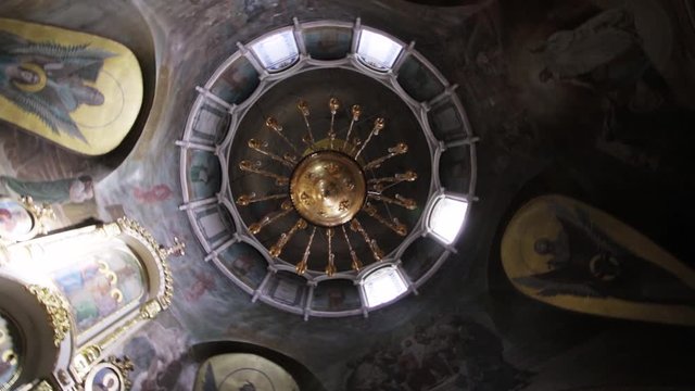 A large golden chandelier weighs under a dome in a church with a painted ceiling
