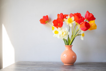 Vase with red white and yellow flowers on a background of a gray wall