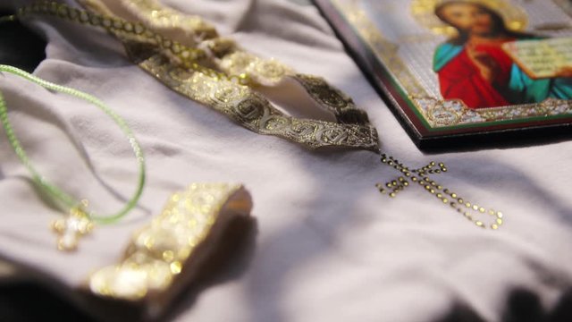 Icon with the face of a saint and a gold cross with a chain lies on a white shirt with gold embroidery for baptism