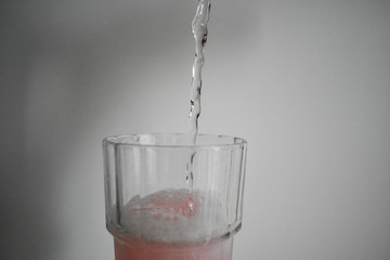 Transparent, pinkish gaseous liquid, falling into a crystal glass foaming