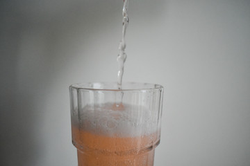 Transparent, pinkish gaseous liquid, falling into a crystal glass foaming