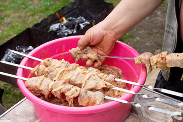 A man puts on raw pork meat for barbecue on skewers for cooking meat on a grilled fire in little village