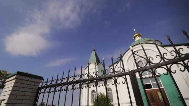 White church with a golden dome and a cross behind a black fence against a blue sky
