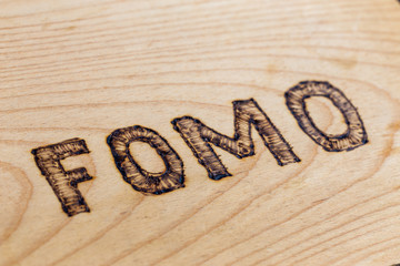Abbreviation FOMO - fear of missing out - burnt by hand on flat wooden surface. Diagonal view with...