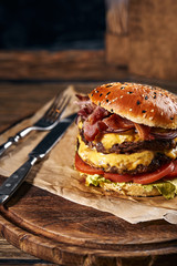 Delicious cheeseburger with salad ingredients on a grilled beef patty served on a crusty golden bread roll on a rustic wooden table with copyspace
