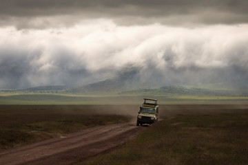 Safari car on a road in Ngorongoro National Park, Tanzania with beautiful clouds in background. Wild nature of Africa.
