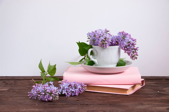 White cup with lilac and pink books on a dark wooden table. Home interior with decoration elements.