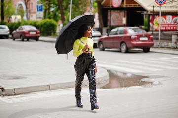 Portrait of young beautiful african american woman holding black umbrella and walking crosswalk.