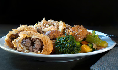 Chicken with broccoli, egg rolls and fried rice, traditional Cantonese Chinese food on a white plate in a black background
