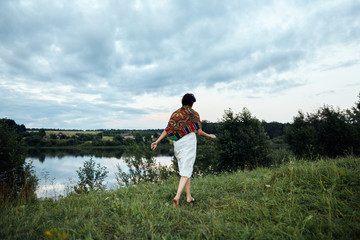 A girl runs along a lush green field to a pond