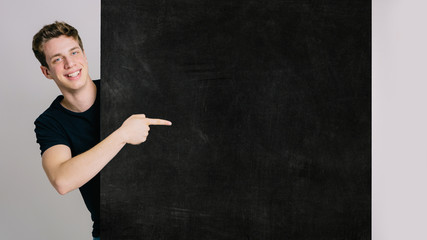 Young blue-eyed boy on an isolated white background shows a customizable billboard with text with his index finger. Space for text, customizable text.