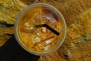 Top view of a plastic cup of iced cappuccino coffee on brown stone.