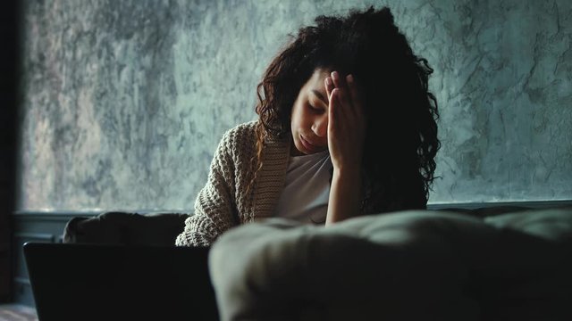 Portrait of young african american woman feeling disappointed reading news using laptop at home. Dark cinematic look