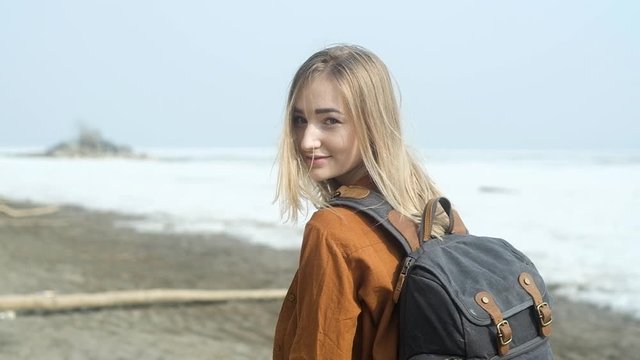 travel along the seacoast. A young Stylish beautiful girl with a backpack on her back travels along a sandy empty beach on a Sunny day.A girl walks on the beach. Active weekend in nature