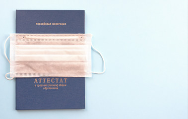 Certificate of graduation and a medical mask on a blue background. The inscription in Russian, the translation is " the Russian Federation. Certificate of secondary (full) General education". 