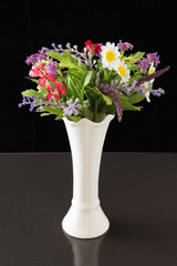 Artificial flowers in a white vase. A bouquet of artificial flowers in a white vase on a black background.