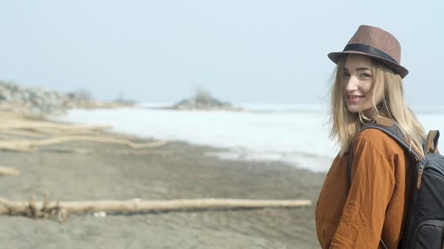 young Stylish beautiful hipster girl in casual clothes in hat with backpack on  back strolls along sandy empty beach while on vacation. Travel to sea on an active weekend. girl walks on the beach.