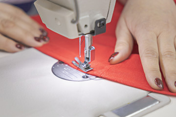 The master sews on a sewing machine. The master is sewing red fabric on a sewing machine. Closeup