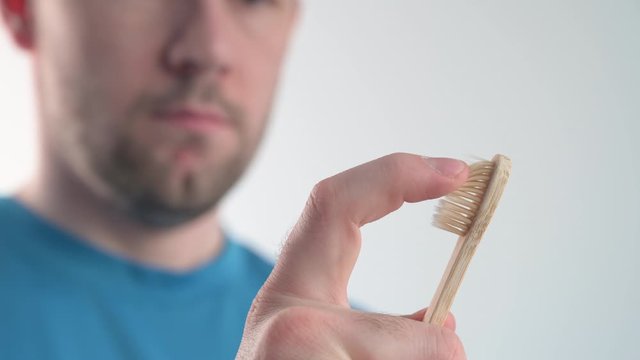 Caucasian adult man swipes a finger on the bristles of a bamboo toothbrush. Zero waste
