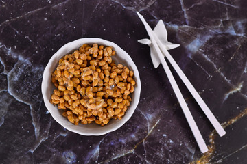Top view of Japanese 'natto', a traditional Japanese food made from fermented soybeans in bowl with chopsticks on dark background