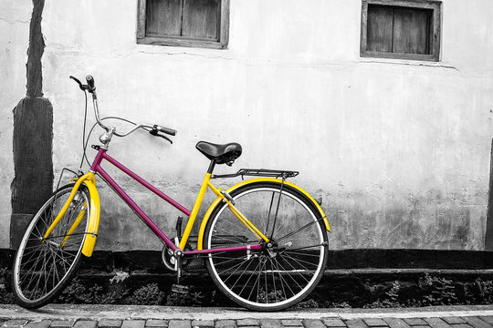 An old yellow bicycle stands against a wall in one of the European streets. The image of the bicycle is made in color. The background is black and white. Place for text on the left side