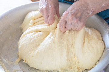 Kneading the dough in home. 
Hands of an elderly woman knead the dough in her home. 