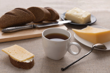 Sliced bread and knife on a cutting board. Butter, cheese, a cup of coffee on a sackcloth. Side view breakfast brunch on table concept