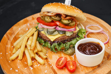 Combo set of fast food. Juicy hamburger, French fries, chicken legs and sauce. Served wooden board and cutlery on a black background. Fast food restaurant. Food delivery.
