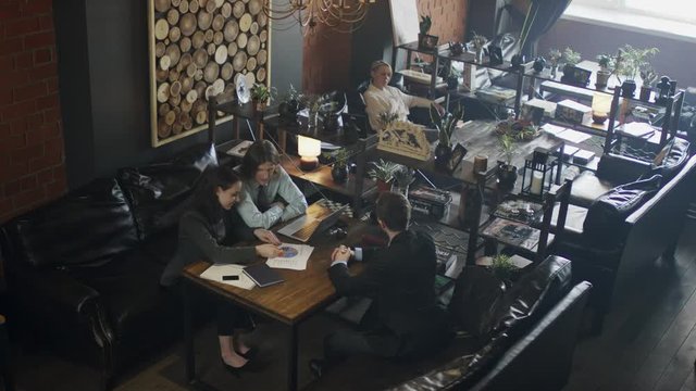 Team of business people looking at pie and bar charts and talking about recent changes in company activities while having meeting in public place.