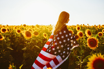 4th of July. Nice girl with the American flag in a sunflower field.Freedom. Sunset light. Independence Day. Patriotic concept.