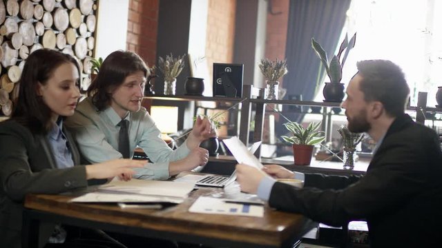 Work team consisting of two men and one woman meeting in public place to debate about project perspectives and examine relevant documents.